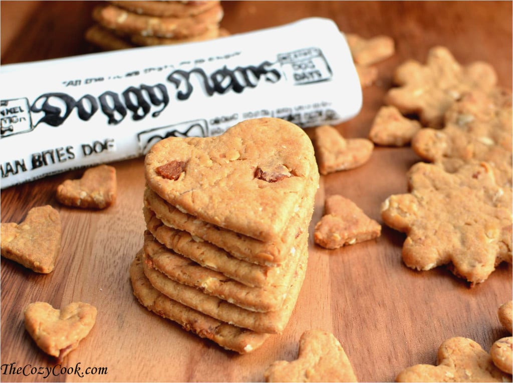 Your four legged friend will love you for this! These treats are filled with savory peanut butter, bacon, oats, and other all-natural ingredients. A stack of heart shaped dog greats on a wooden surface surrounded by smaller dog treats with a toy newspaper in background.