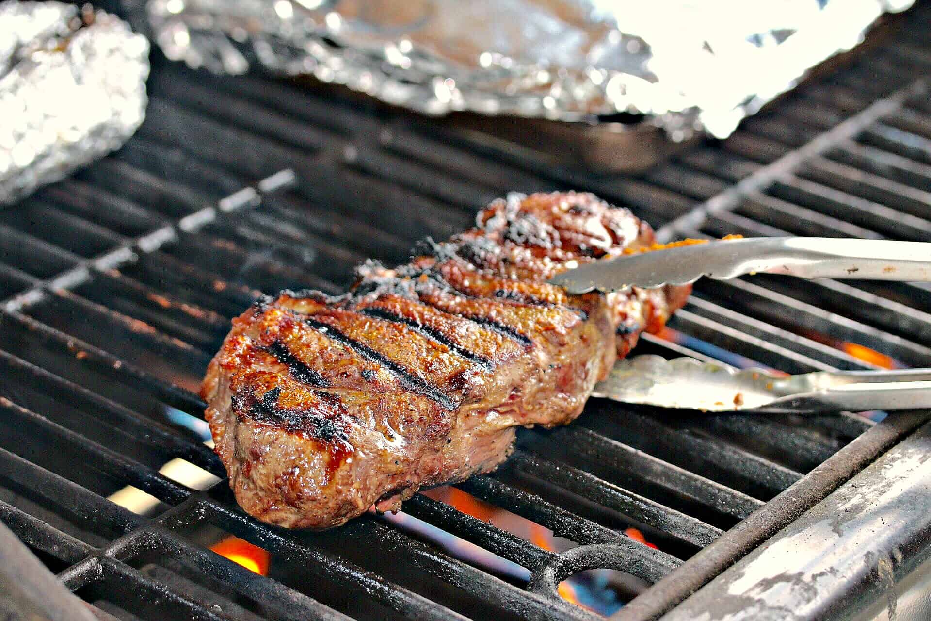 A simple combination of ingredients will bring out the best flavors in your chicken or steak, and tastes just like the Texas Roadhouse restaurant! A seasoned steak on a grill with kitchen tongs lifting it up.