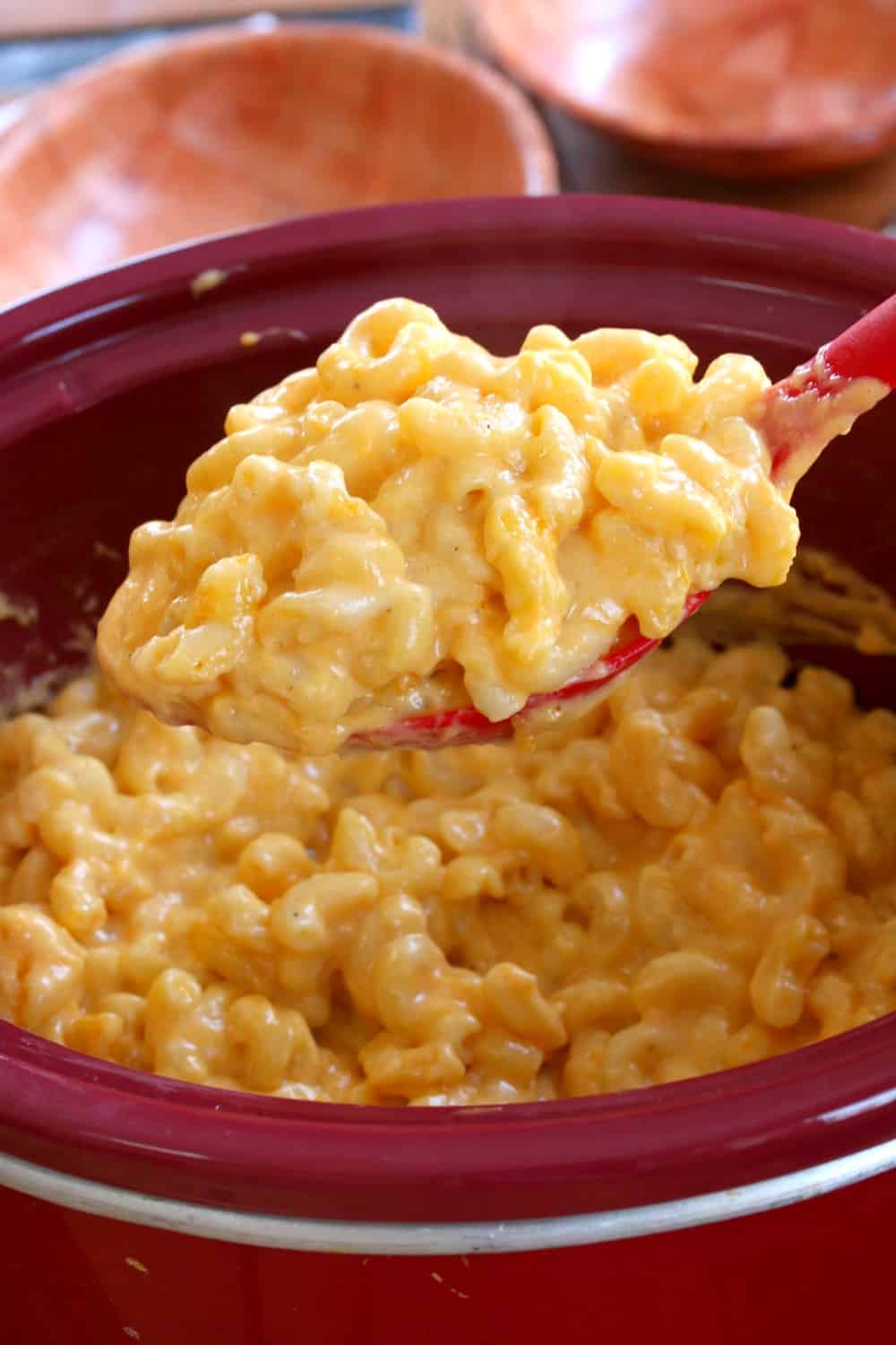 This extra creamy crock pot mac and cheese is easy to make & a universal crowd-pleaser! It takes minutes to prepare and the crock pot does the rest. Large spoon full of macaroni and cheese scooped up from a red crock pot.