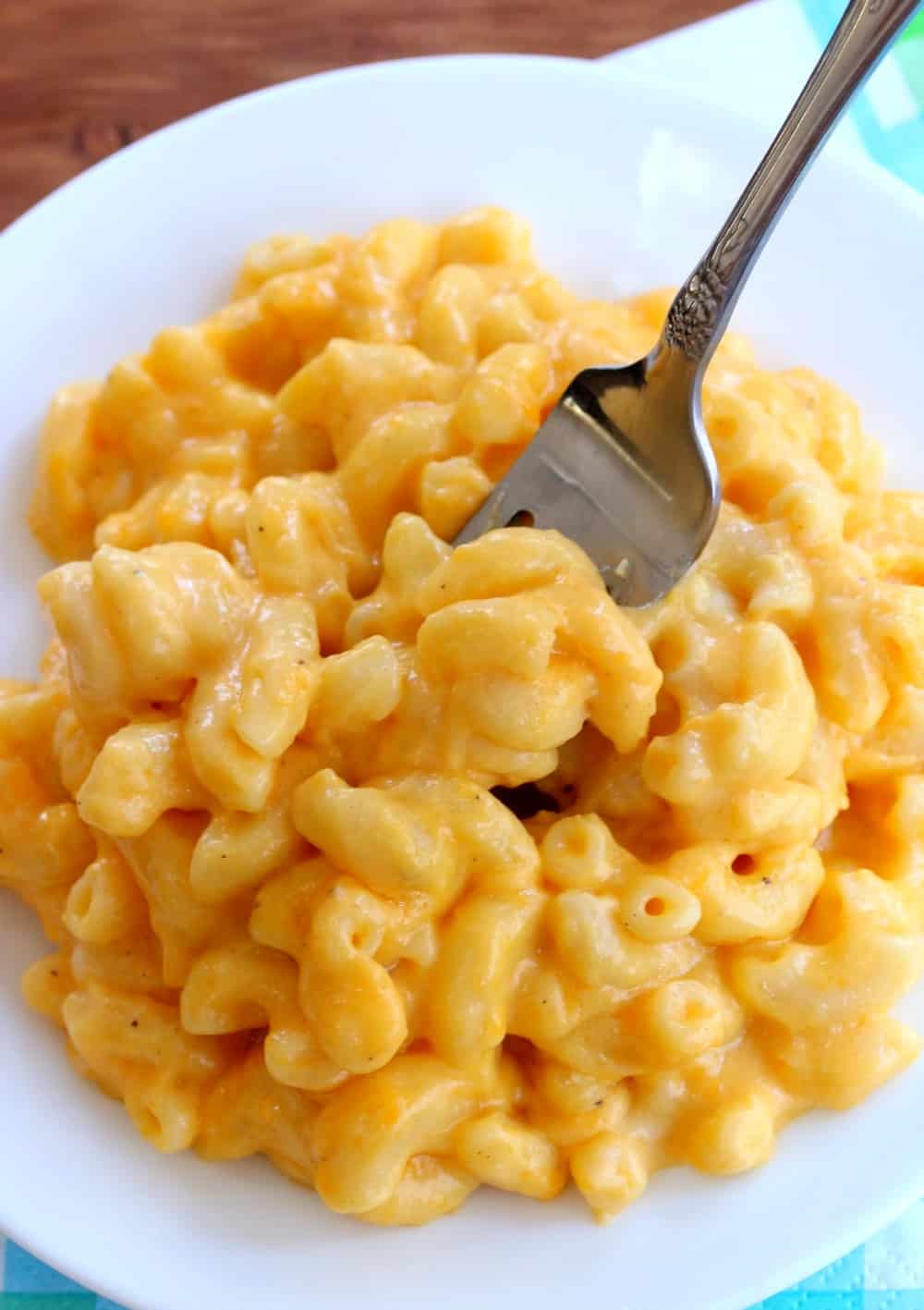 This extra creamy crock pot mac and cheese is easy to make & a universal crowd-pleaser! It takes minutes to prepare and the crock pot does the rest. White plate full of macaroni and cheese with fork inserted into it.