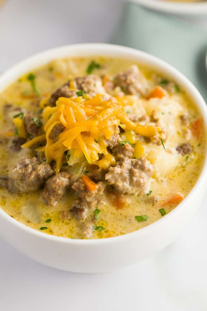 This slow cooker cheeseburger soup is loaded with tender ground beef and vegetables in a thick and creamy cheesy soup, the definition of comfort in a bowl! Close up of Crock Pot Cheeseburger Soup with grated cheese on top.