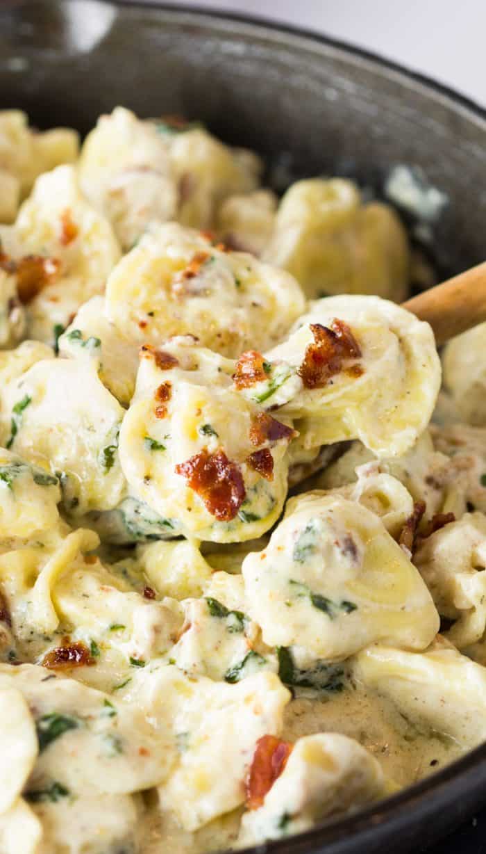 This Tortellini Al Forno features stuffed tortellini tossed in a rich and creamy garlic cheese sauce and topped with crumbled bacon. | The Cozy Cook | #Tortellini #Pasta #OliveGarden #AlForno #Dinner, #Cheese #Parmesan #Bacon A cast iron skillet filled with tortellini in a cream sauce with bacon sprinkled on top.