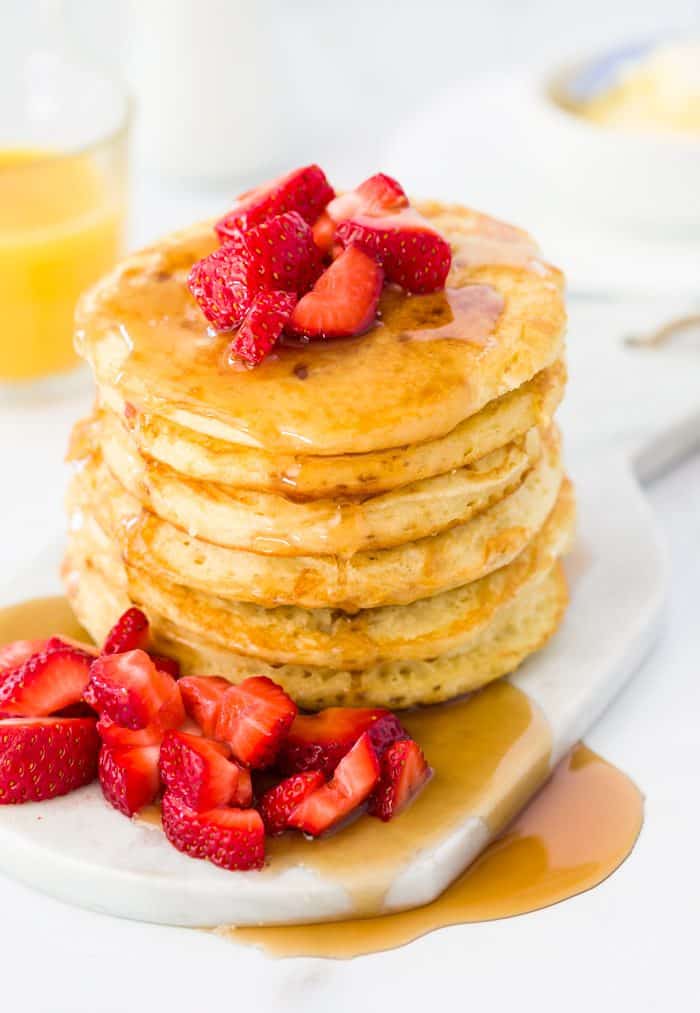 Sweet and fluffy pancakes served with fresh fruit and warm syrup. They taste just like IHOP's classic buttermilk pancakes, but are even better made at home! A tall stack of buttermilk pancakes topped with diced strawberries with a glass of orange juice in the background.
