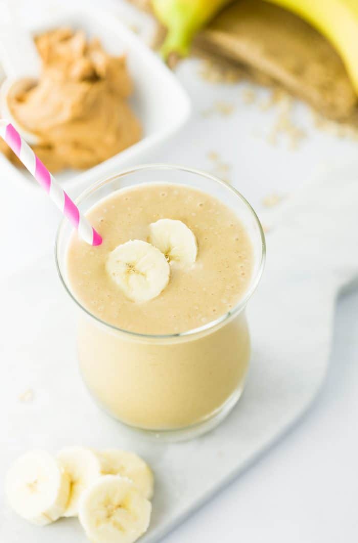 Smooth peanut butter combined with a refreshing frozen banana, milk of choice, and a splash of vanilla. This energizing smoothie is healthy and satisfying! overhead image of a peanut butter banana smoothie in a glass with a scoop of peanut butter and bananas in the background.