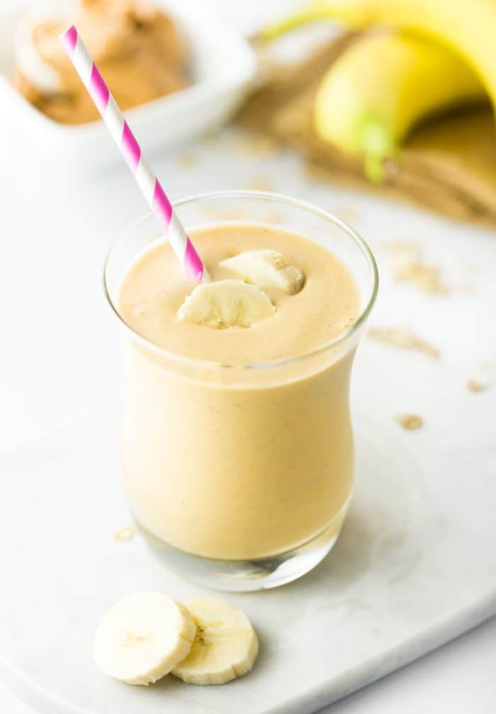 Smooth peanut butter combined with a refreshing frozen banana, milk of choice, and a splash of vanilla. This energizing smoothie is healthy and satisfying! A glass cup with a Peanut Butter Banana Smoothie topped with two sliced bananas with a pink and white straw.