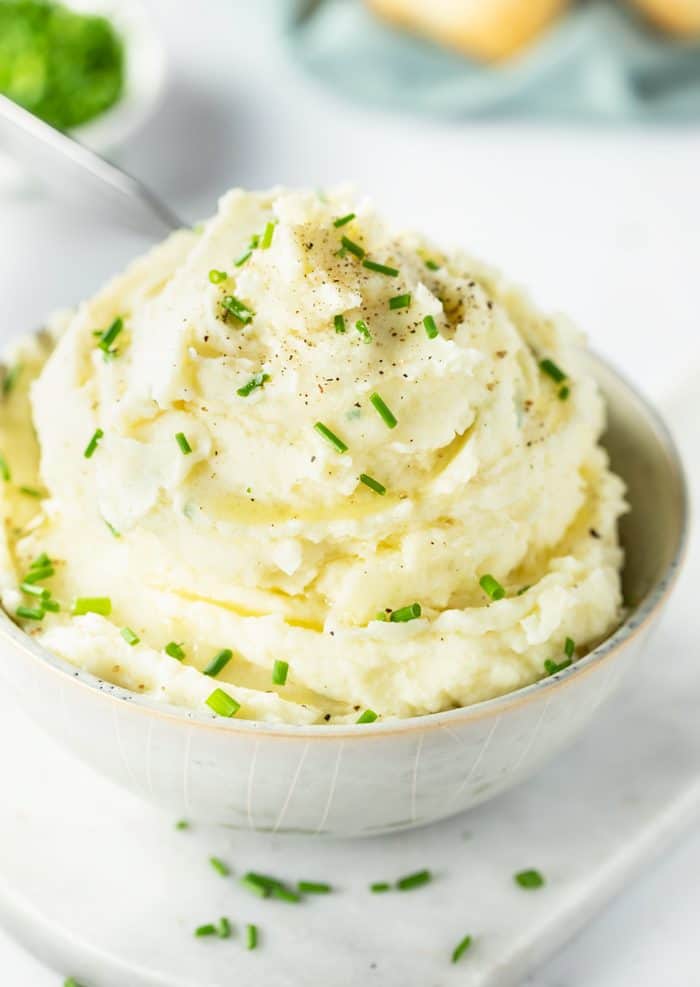 The creamiest mashed potatoes you'll ever try, made right in the Instant Pot! Free up your stove for the main meal while you prepare this savory side that the instant pot will keep warm for you! Mashed Potatoes in a small bowl topped with chopped chives and pepper.