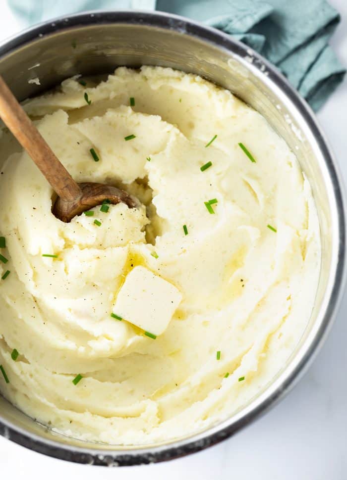 The creamiest mashed potatoes you'll ever try, made right in the Instant Pot! Free up your stove for the main meal while you prepare this savory side that the instant pot will keep warm for you! Instant Pot Filled with Mashed Potatoes topped with butter with a wooden spoon.