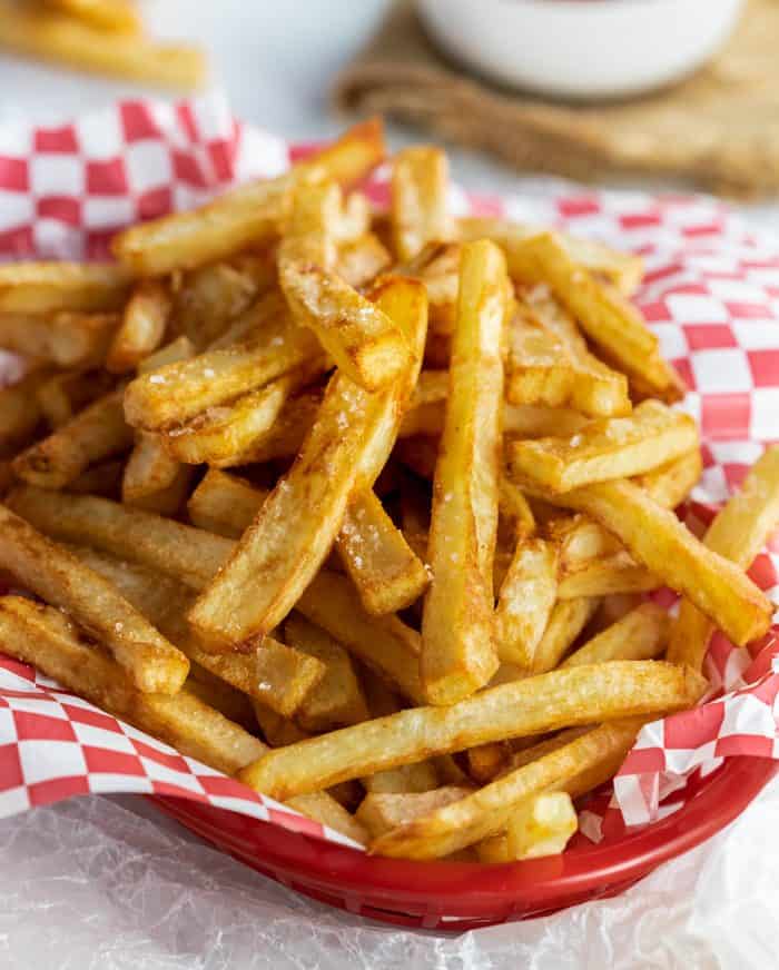 Learn the secret to making the best homemade french fries from russet potatoes! These are easy to make ahead of time and fry or bake in the oven for a quick snack or side dish idea! #baked #potatorecipe #friedfood #snackideas #fromscatch A pile of crispy, golden brown french fries in a basket sprinkled with salt.