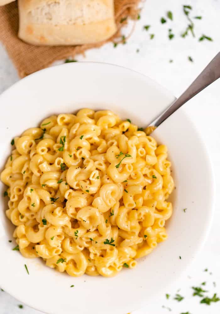 This super creamy Instant Pot macaroni and cheese cooks in just 5 minutes with only a single pot to clean! Your whole family will love this extra easy, cheesy meal! | The Cozy Cook | #macaroni #cheese #instantpot #dinner #pasta A bowl of macaroni and cheese with chopped parsley sprinkled on top and around the bowl.