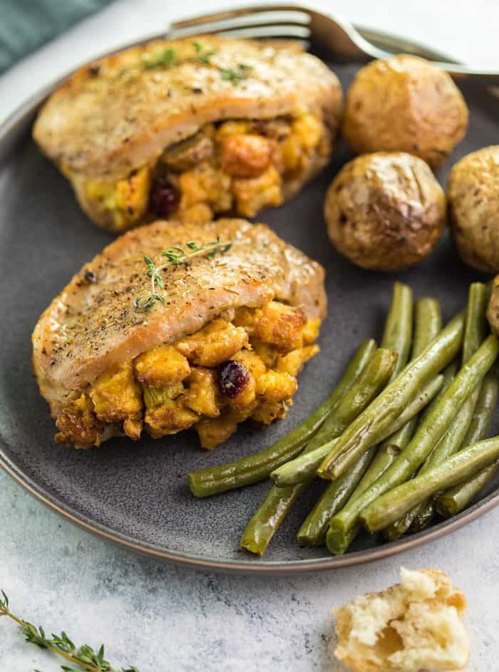 These easy-to-make Pork Chops are perfectly seasoned and stuffed with delicious sausage cranberry stuffing. They are then baked to perfection in just 20 minutes and pair perfectly with roasted potatoes and green beans. | The Cozy Cook | #PorkChops #Dinner Golden brown pork chops filled with golden stuffing on a plate with green beans and roasted potatoes