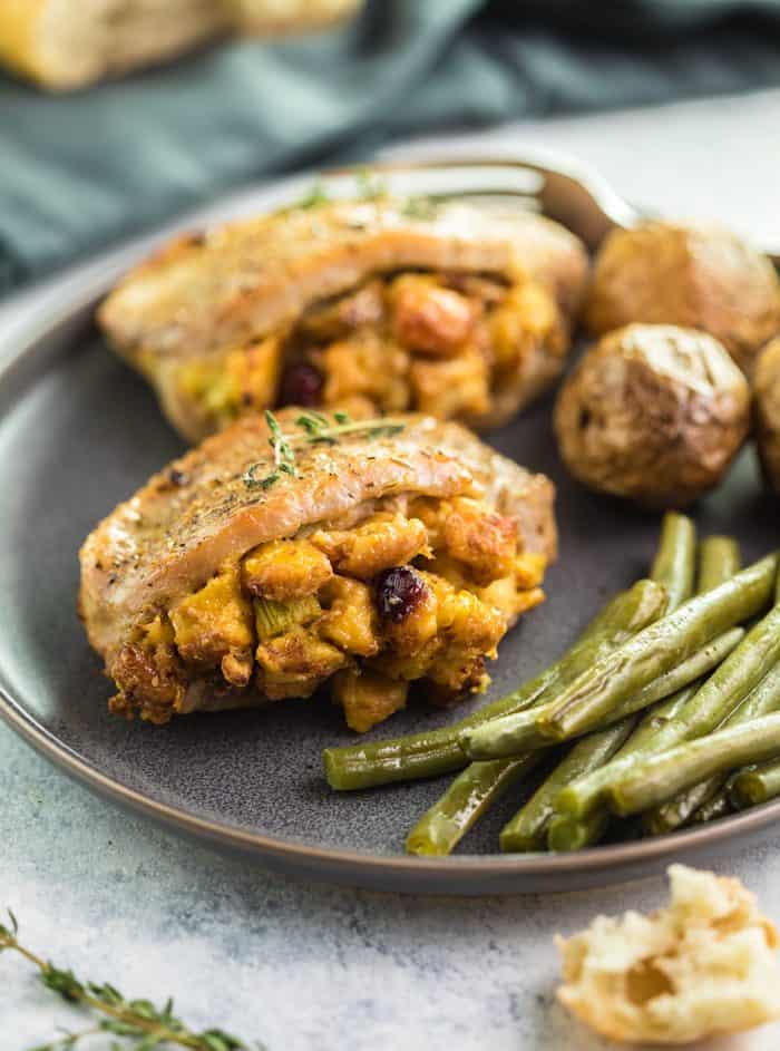These easy-to-make Pork Chops are perfectly seasoned and stuffed with delicious sausage cranberry stuffing. They are then baked to perfection in just 20 minutes and pair perfectly with roasted potatoes and green beans. | The Cozy Cook | #PorkChops #Dinner Seasoned Baked Pork Chops filled with Stuffing on a plate with green beans and roasted potatoes