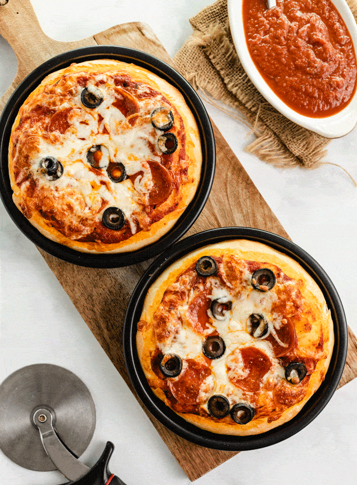 Overhead shot of 2 Pizza Hut Pizzas on wooden cutting board after being baked.