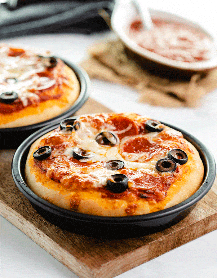 6 inch Pizza Hut Personal Pan Pizza in Pizza pan on wooden cutting board with another pizza and sauce behind it.