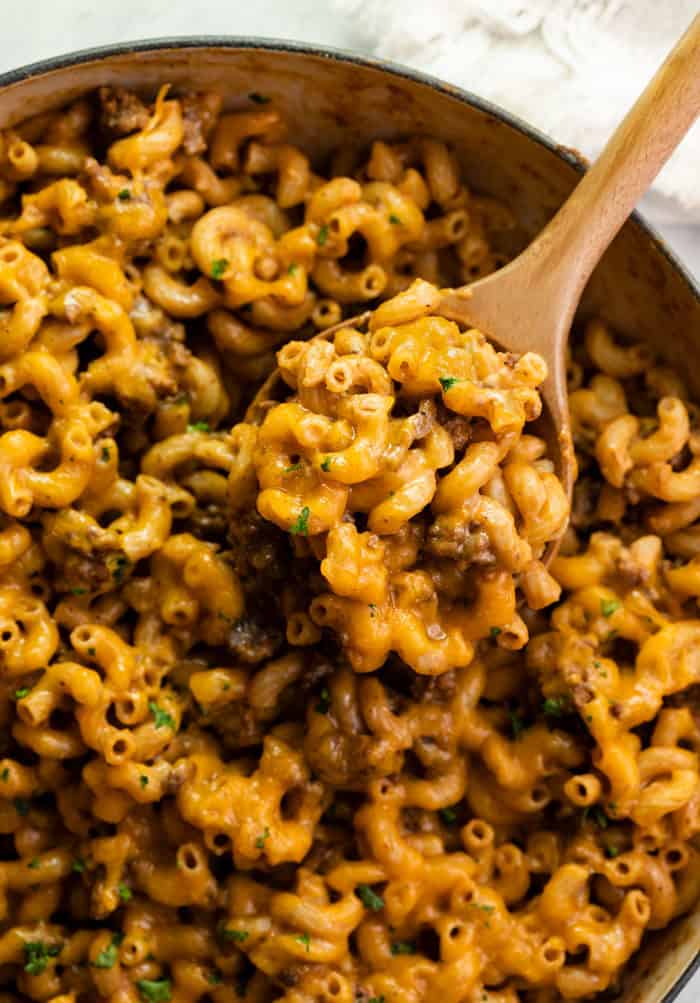 This Cheeseburger Casserole is made in one pot and takes just 30 minutes! It's a cheesy, meaty, and easy macaroni dinner. A homemade version of Hamburger Helper! #comfortfood #pasta #familydinneridea #dinnersforkids overhead view of a skillet filled with cheeseburger casserole and a wooden spoon scooping it out.