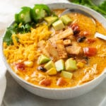 A bowl of Creamy Chicken Tortilla Soup topped with crispy tortillas and garnished with avocados, cheese, jalapenos, and cilantro.