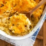 Overhead view of a white casserole dish filled with hashbrown casserole with a wooden spoon scooping it up.
