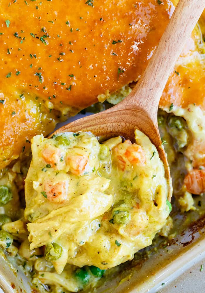 This Bisquick Chicken Pot Pie has a golden biscuit crust and an easy homemade filling that can be prepared two days ahead of time! #casserole #familydinnerideas #comfortfood #dinner #comfortfood #chickendinnerideas #mealprep #makeahead Wooden spoon scooping out chicken pot pie filling from a casserole dish.