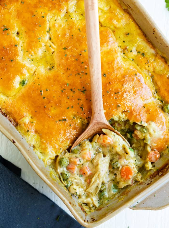 This Bisquick Chicken Pot Pie has a golden biscuit crust and an easy homemade filling that can be prepared two days ahead of time! #casserole #familydinnerideas #comfortfood #dinner #comfortfood #chickendinnerideas #mealprep #makeahead Chicken Pot Pie Casserole with a wooden spoon in a casserole dish.