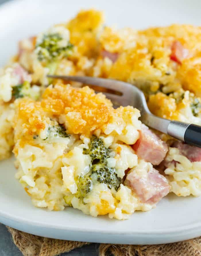 ham casserole with rice and broccoli on a white plate with a fork inserted into it.