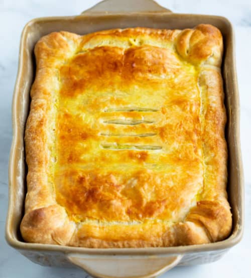 This spinach pie recipe is made with eggs, caramelized onions, gruyere cheese, and golden puff pastry. An easy side dish idea for Thanksgiving or a family dinner! #makeahead #creamy #sidedishes #holidaysidedish #christmassidedish #vegetablesidedishes #comfortfood A casserole with golden brown puff pastry .
