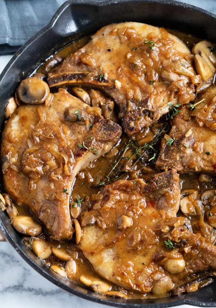 Seasoned Pork Chops are smothered in a thick and flavorful French Onion sauce with gravy and mushrooms. They are pan fried or baked in the oven. Top with hot, melted cheese for extra indulgence! #smotheredporkchops #onepotmeals #mushroomsauce #caramlizedonions #pork Pork Chops in a cast iron skillet smothered with a french onion sauce with mushrooms and gravy.