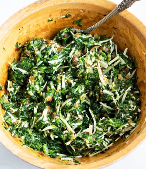This spinach pie recipe is made with eggs, caramelized onions, gruyere cheese, and golden puff pastry. An easy side dish idea for Thanksgiving or a family dinner! #makeahead #creamy #sidedishes #holidaysidedish #christmassidedish #vegetablesidedishes #comfortfood A mixing bowl of spinach pie filling ingredients mixed together.