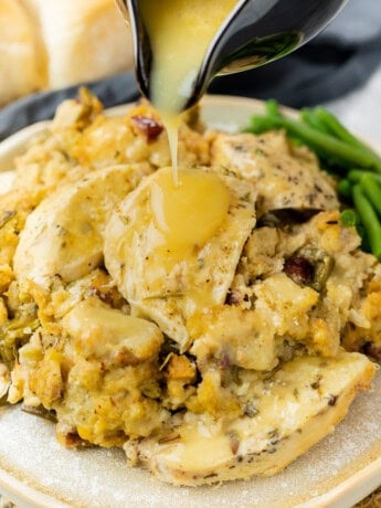 A plate of crock pot chicken and stuffing with gravy being poured on top.