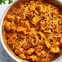 Chicken Scallopini in a skillet with a red wine reduction sauce and pasta.