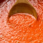 A wooden spoon scooping up homemade marinara sauce from a pot.