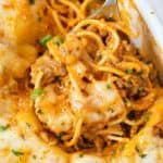 A spoon holding up baked spaghetti from a casserole dish.