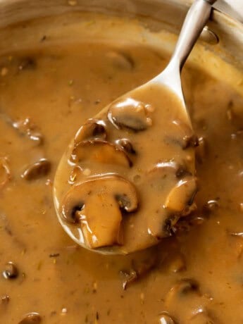 A spoon full of thick and creamy mushroom gravy from a skillet.
