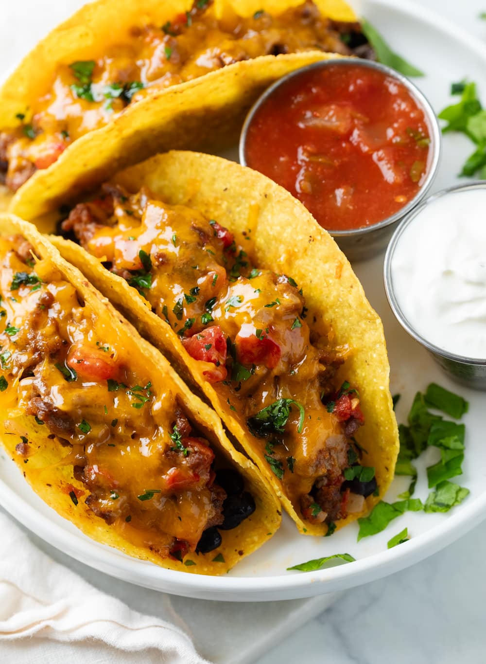 Baked Tacos on a white plate next to salsa and sour cream.