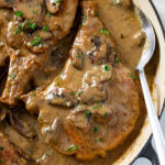 Mushroom Pork Chops in a skillet with gravy and fresh parsley.