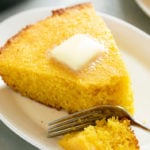 A slice of cornbread on a white plate with butter on top.