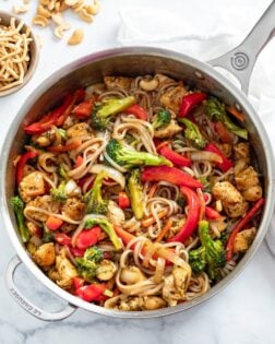 A skillet with Chicken Noodle Stir Fry with Chow Mein Noodles and Cashews on the side.
