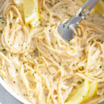A skillet filled with Creamy Herb Pasta with lemon slices and kitchen tongs.