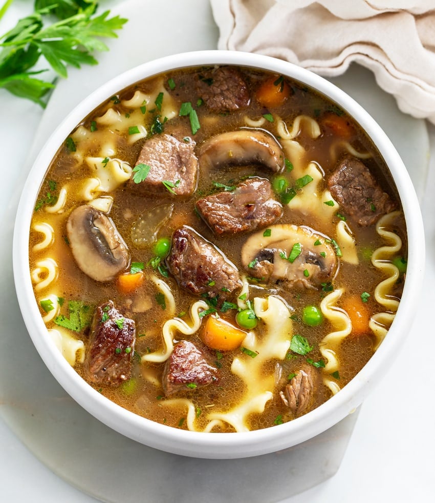 A white bowl of beef noodle soup with parsley on top.