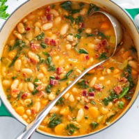 A Dutch oven filled with white bean soup with a ladle in it.