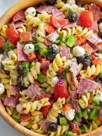 Italian Pasta Salad in a wooden bowl with spiral pasta, cheese, meat, and vegetables.