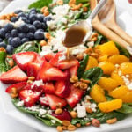 A spinach salad on a white platter with Balsamic Vinaigrette being drizzled on top.
