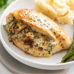 Stuffed Chicken Breast on a white plate with green beans on the side and mashed potatoes in the back.
