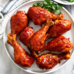 A white plate of Baked BBQ Chicken with parsley on the side.