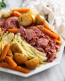 Corned Beef and Cabbage on a white platter with carrots and potatoes.