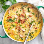 Kielbasa Potato Soup in a soup pot with bacon and green onions on top and a ladle on the side.