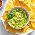 Homemade Guacamole in a bowl with fresh cilantro on the side and tortilla chips around it.