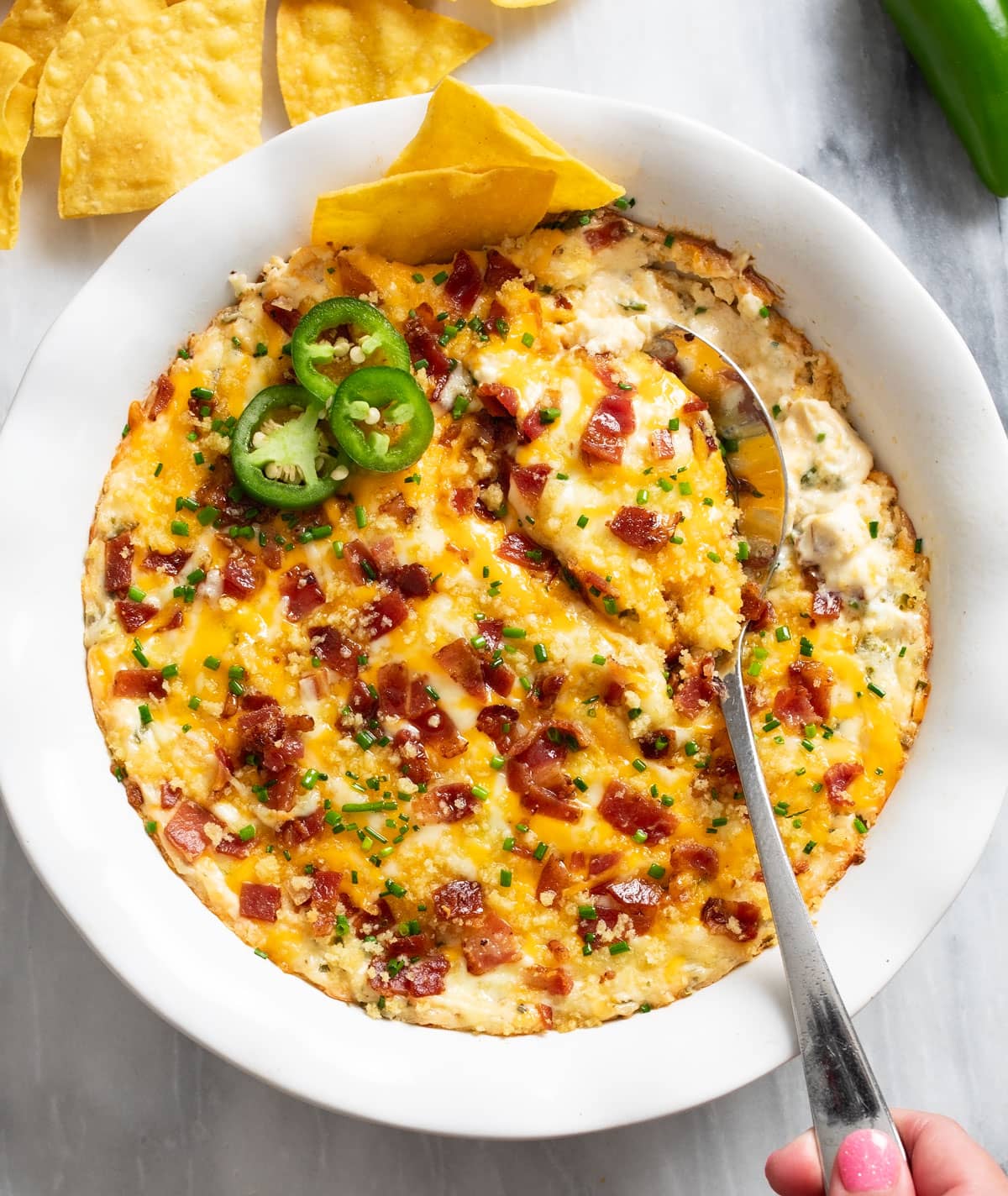 Jalapeno Popper Dip in a white baking dish with a spoon on the side and jalapenos on top.