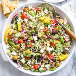 Greek Salad in a white bowl with vegetables, chickpeas, dressing, and feta.