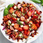 Tomato Salad in a white bowl with mozzarella pearls, fresh basil, red onions, and homemade balsamic dressing.