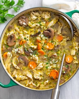 A soup pot with chicken and mushroom soup with rice in it and a ladle on the side.