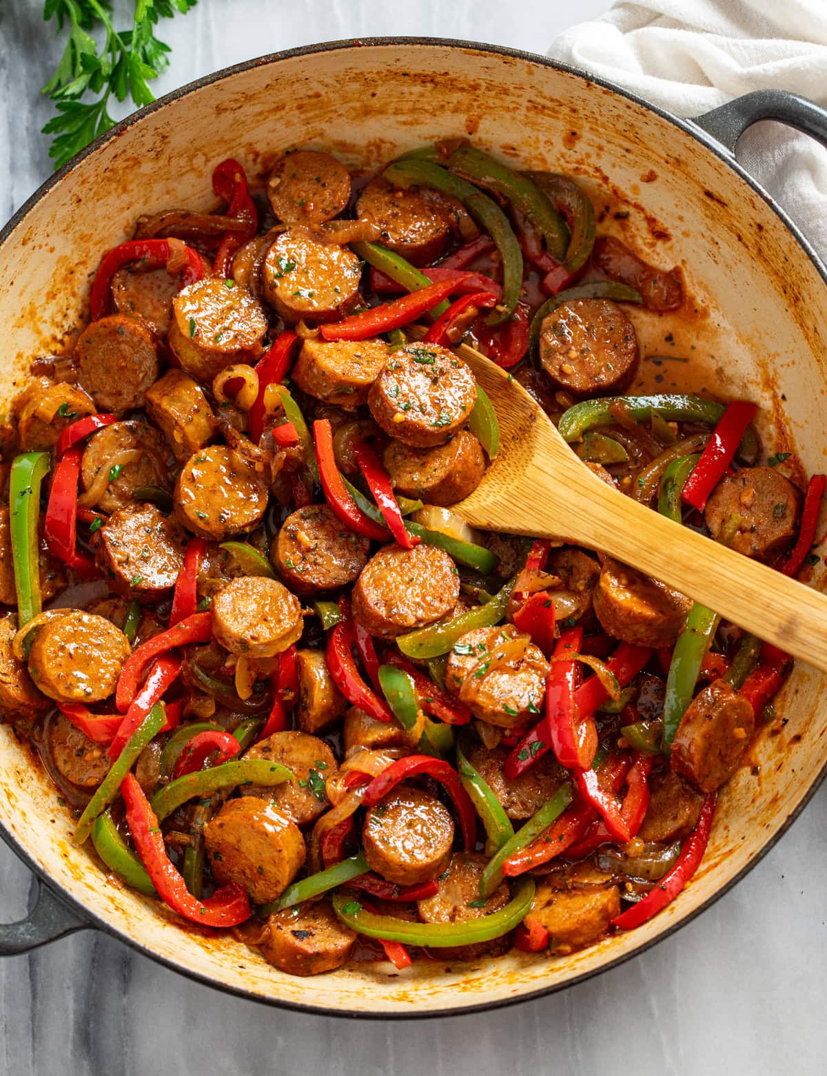 Overhead view of Sausage and Peppers in a skillet with a wooden spoon in the middle.
